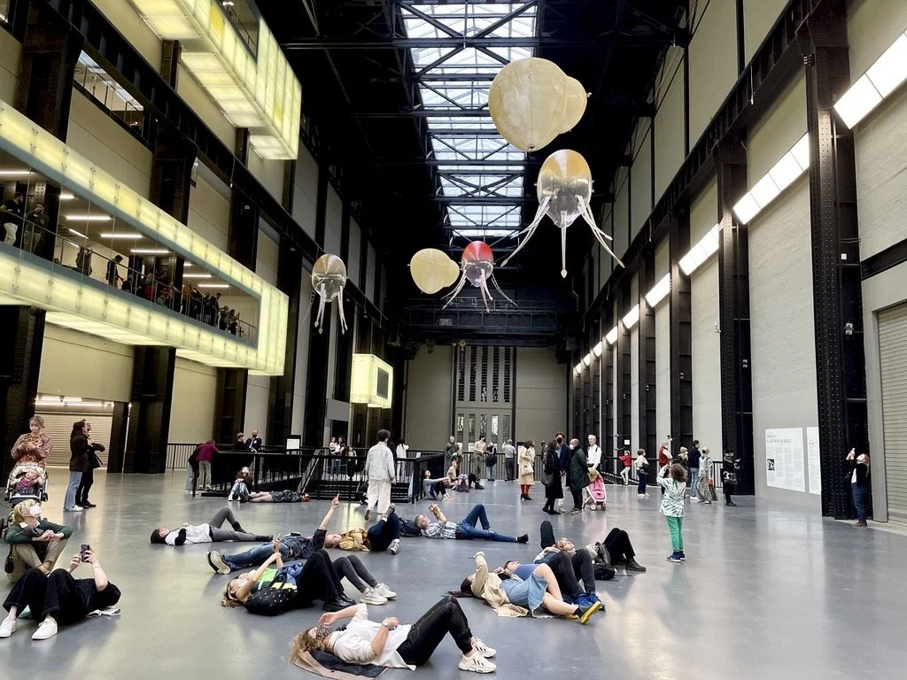 Visitors lying on the Turbine Hall floor watching multiple aerobes fly overhead