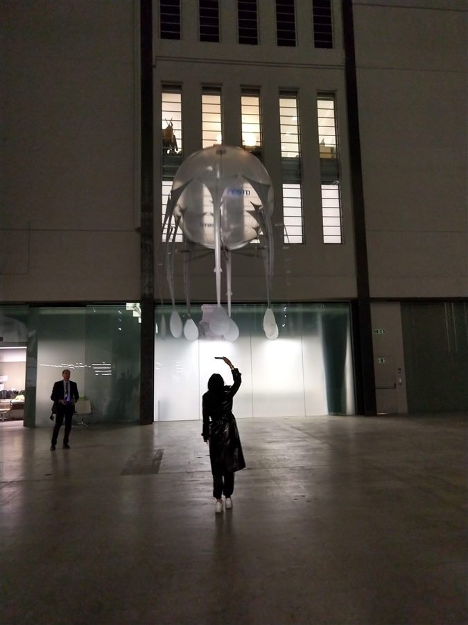 A visitor photographing a single aerobe hovering near the Turbine Hall entrance at night