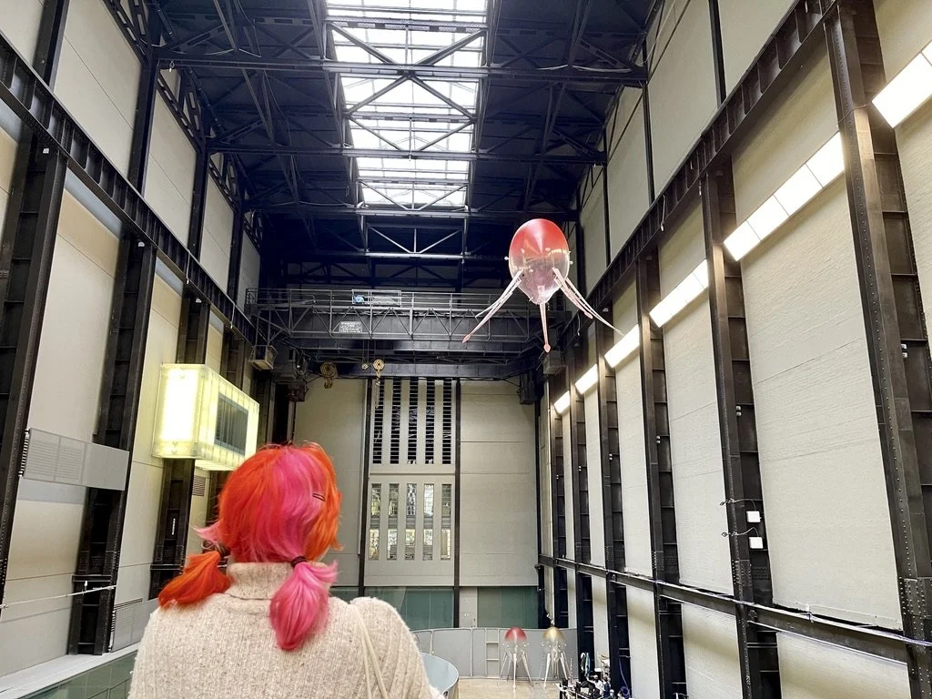 A visitor watching a single aerobe hovering close overhead at Tate Modern